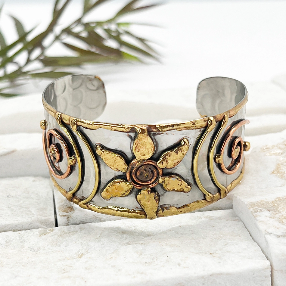 Wide silver, brass and copper cuff bracelet with flower and spiral accents.