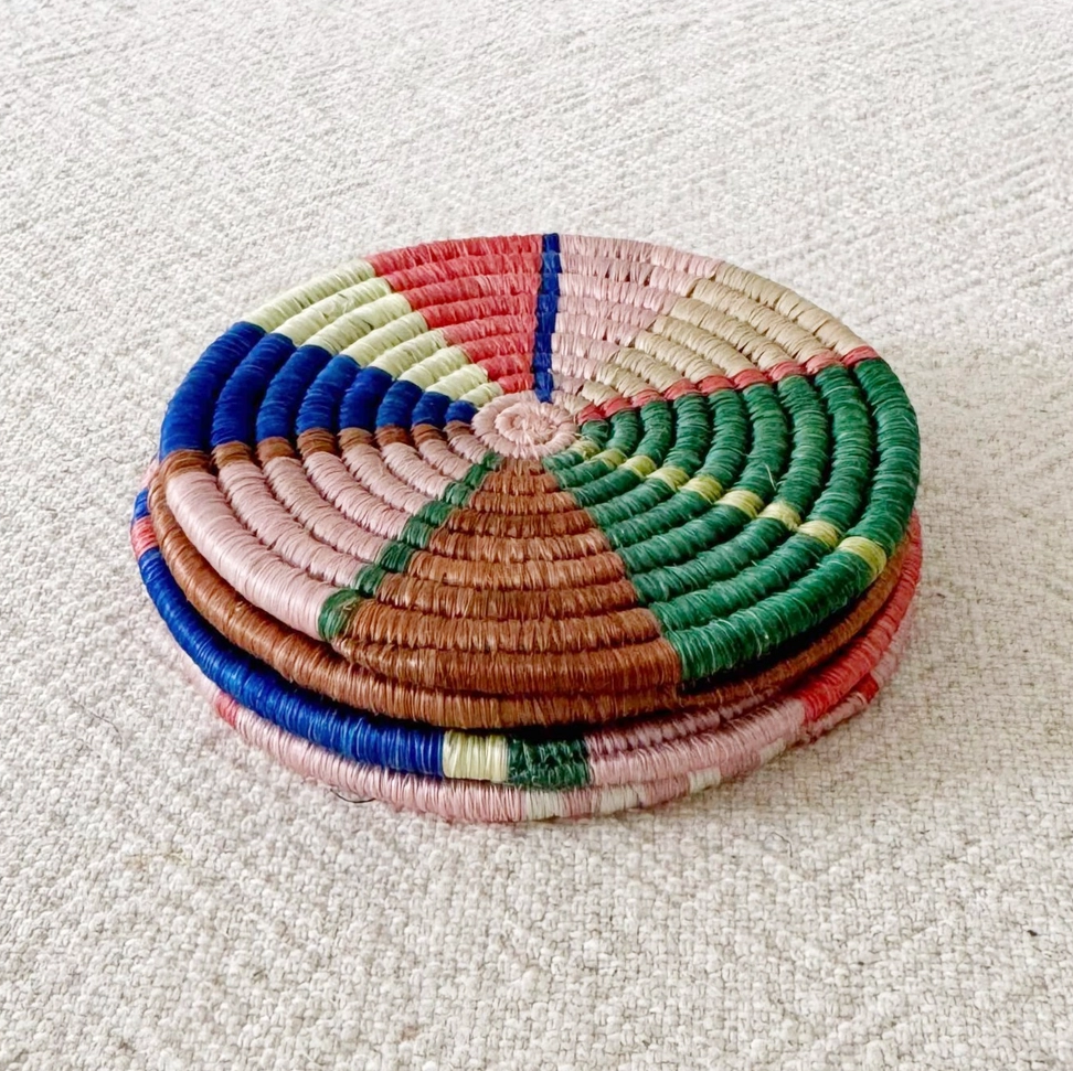 Set of 4 round handwoven coaster in pink, green, blue brown geometric pattern stacked.