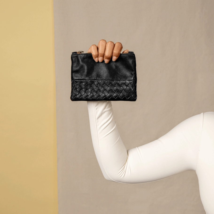 Model holding small black leather pouch with woven design on front.