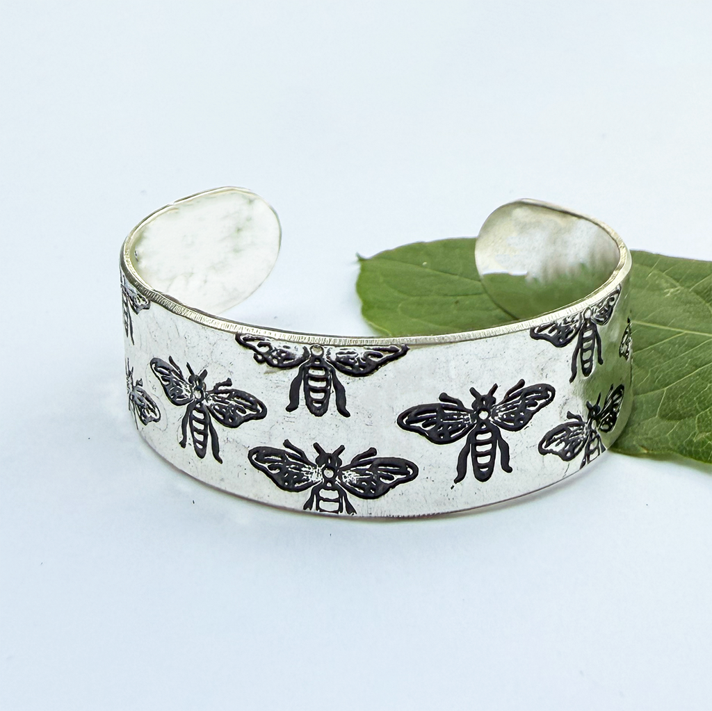 Silver cuff bracelet with bees on it in black