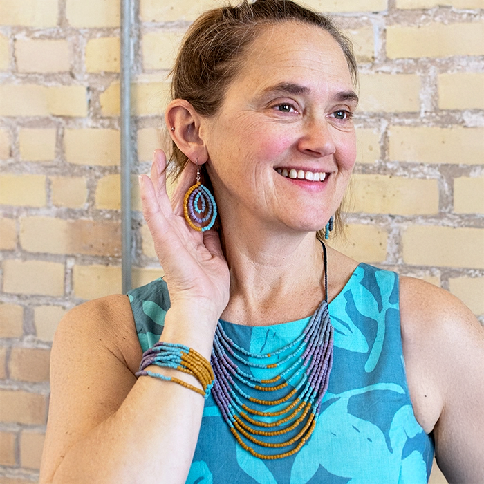 Glass statement necklace, earrings and bracelet on model with several strand of beads in gold, purple and blue