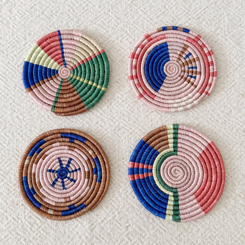 Set of 4 round handwoven coaster in pink, green, blue brown geometric pattern.