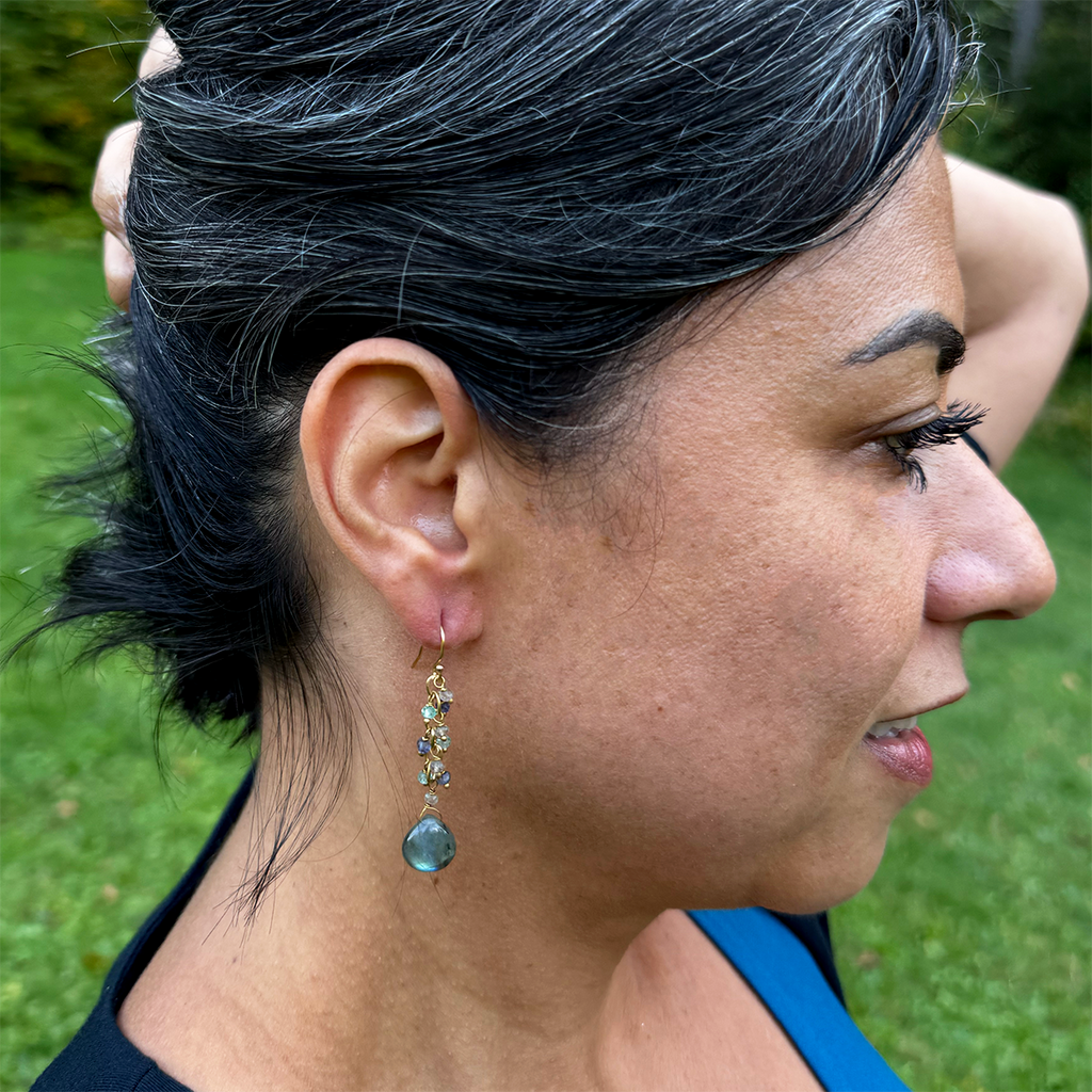 Earrings on model with a cluster of tiny labradorite stones and one teardrop shaped larger stone on the bottom with brass.