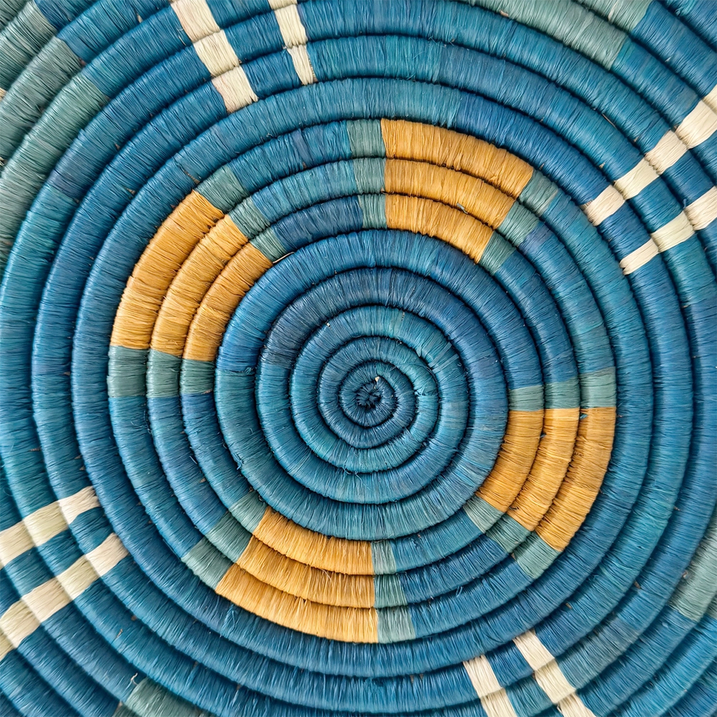 Round handwoven trivet with geometric design with blue green white and orange close up