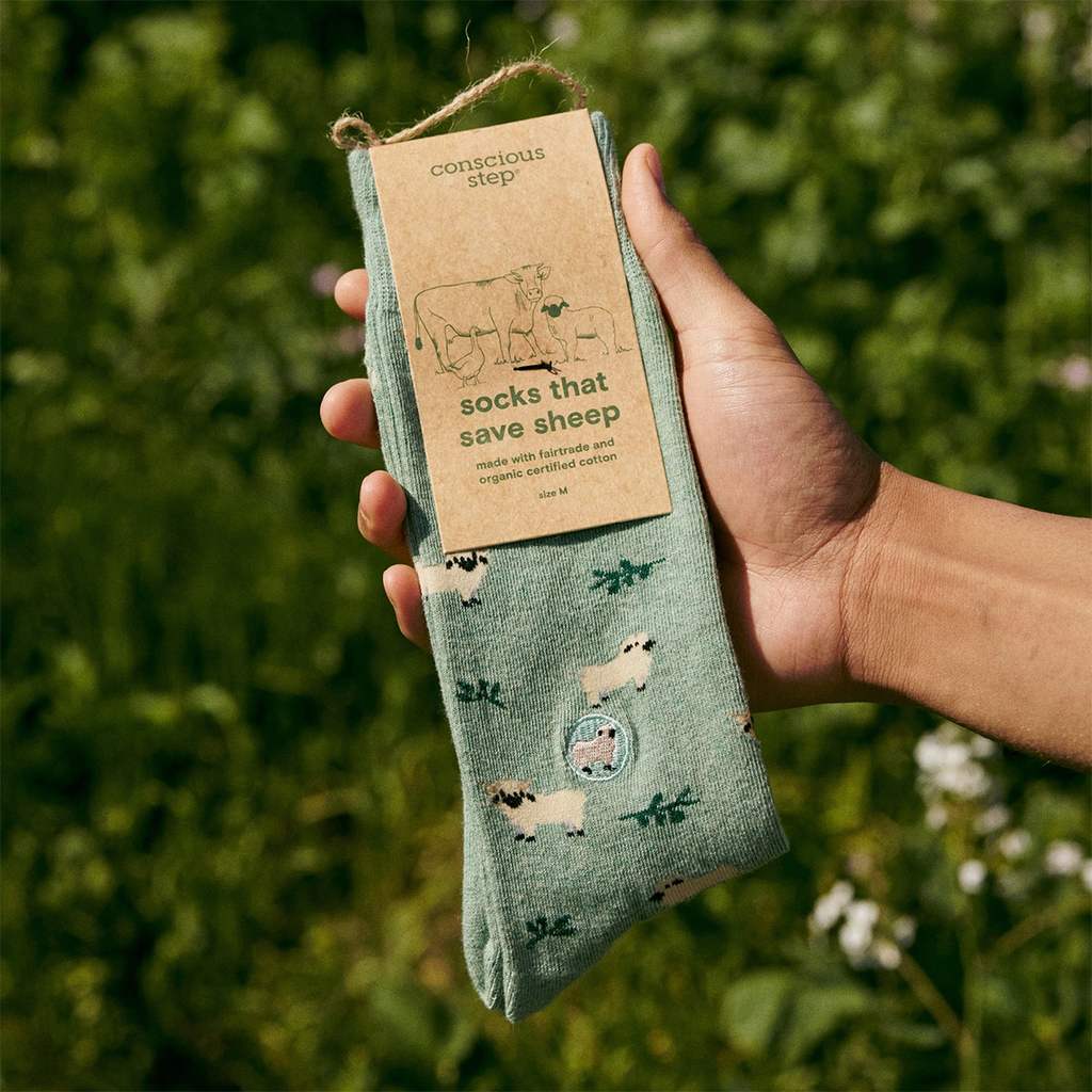 Light green socks with sheep and tag that says Socks That Save Sheep.