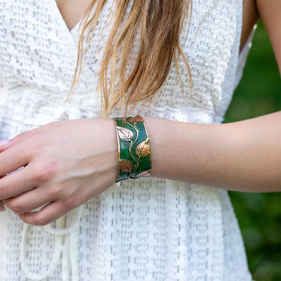 Fair trade cuff bracelet with green base and brass leaves on top.