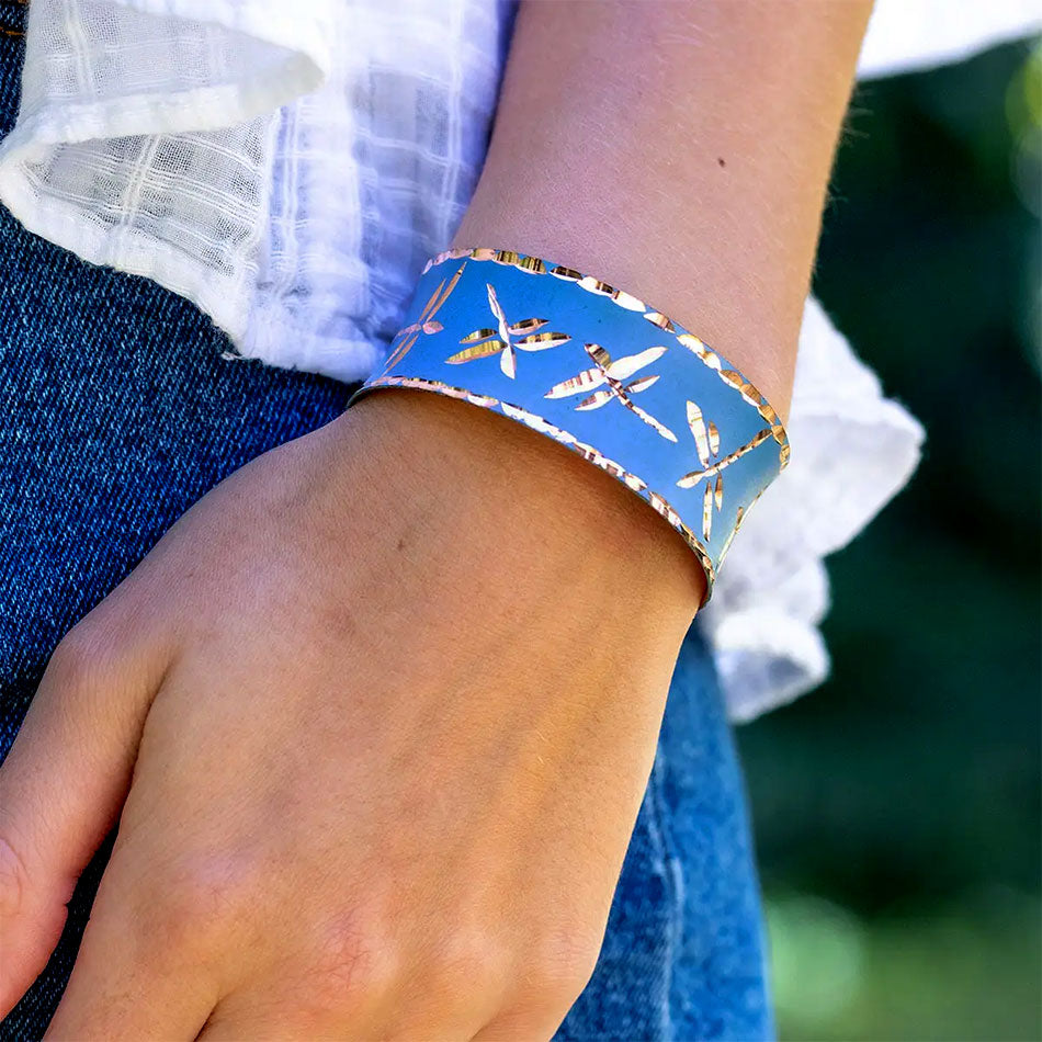 Fair trade copper cuff bracelet with dragonfly design on blue.
