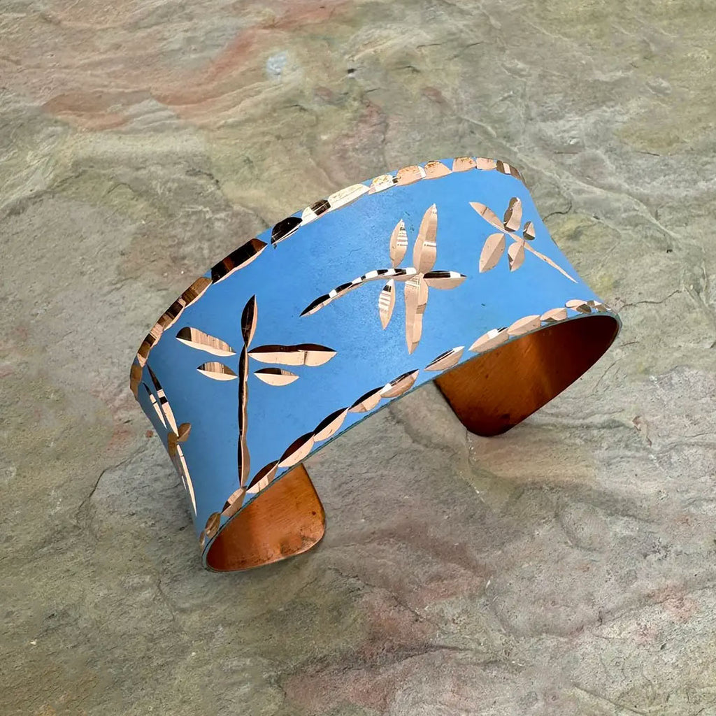 Fair trade copper cuff bracelet with dragonfly design on blue.